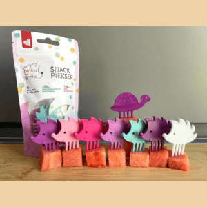 Set aus sieben Snack-Pieksern in Igel-Form in pink/lila Tönen sowie einer lila Schildkröte, sie sind in einer Reihe aufgestellt, jeweils in ein Stück Melone gepiekst.