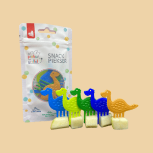 Zu sehen ist das Set "big five" aus fünf Snack Pieksern in Dinosaurier-Form (in den Farben blau, gelbgrün, blattgrün, ultramarine und braun), in einer Reihe jeweils in ein Apfelwürfel gesteckt, daneben außerdem die Verpackung der Snack Piekser Dinosaurier.